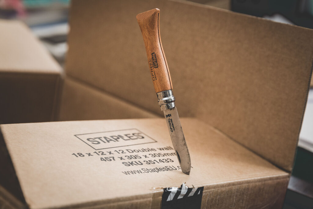 Opinel knife dropped point-first in the lid of a cardboard box